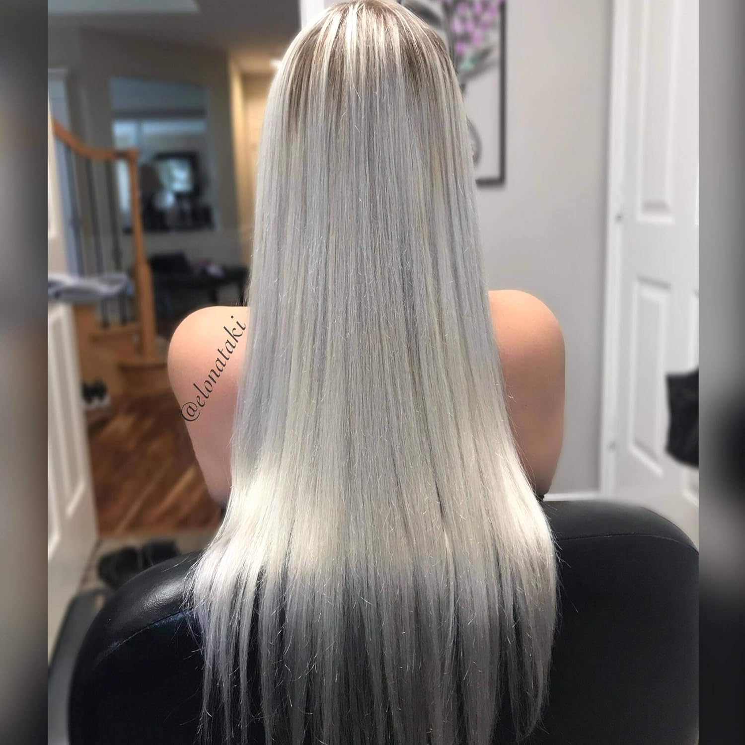 Back view of long, straight, platinum blonde hair with darker tips, indoors with a white door and framed picture.