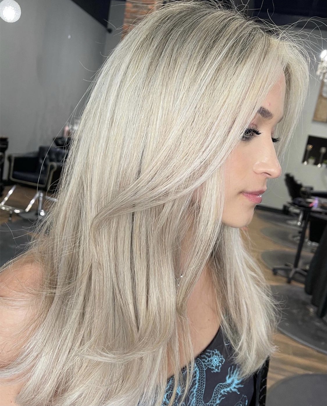 Side profile of a woman with long, straight, platinum blonde hair in a salon setting.