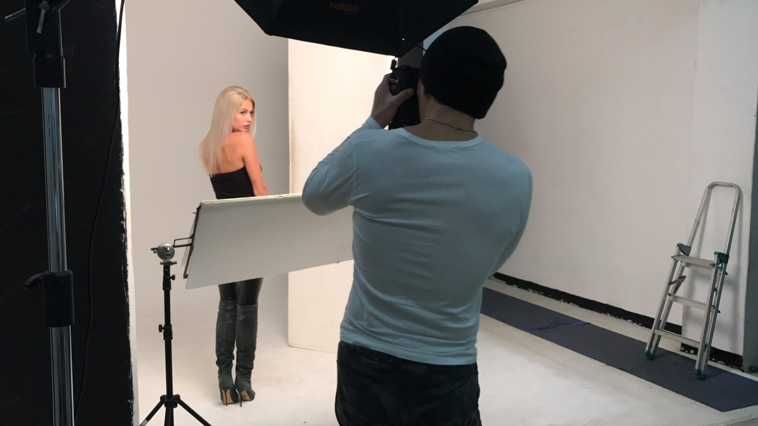 Photographer taking a picture of a woman in a studio with white walls and a ladder nearby.