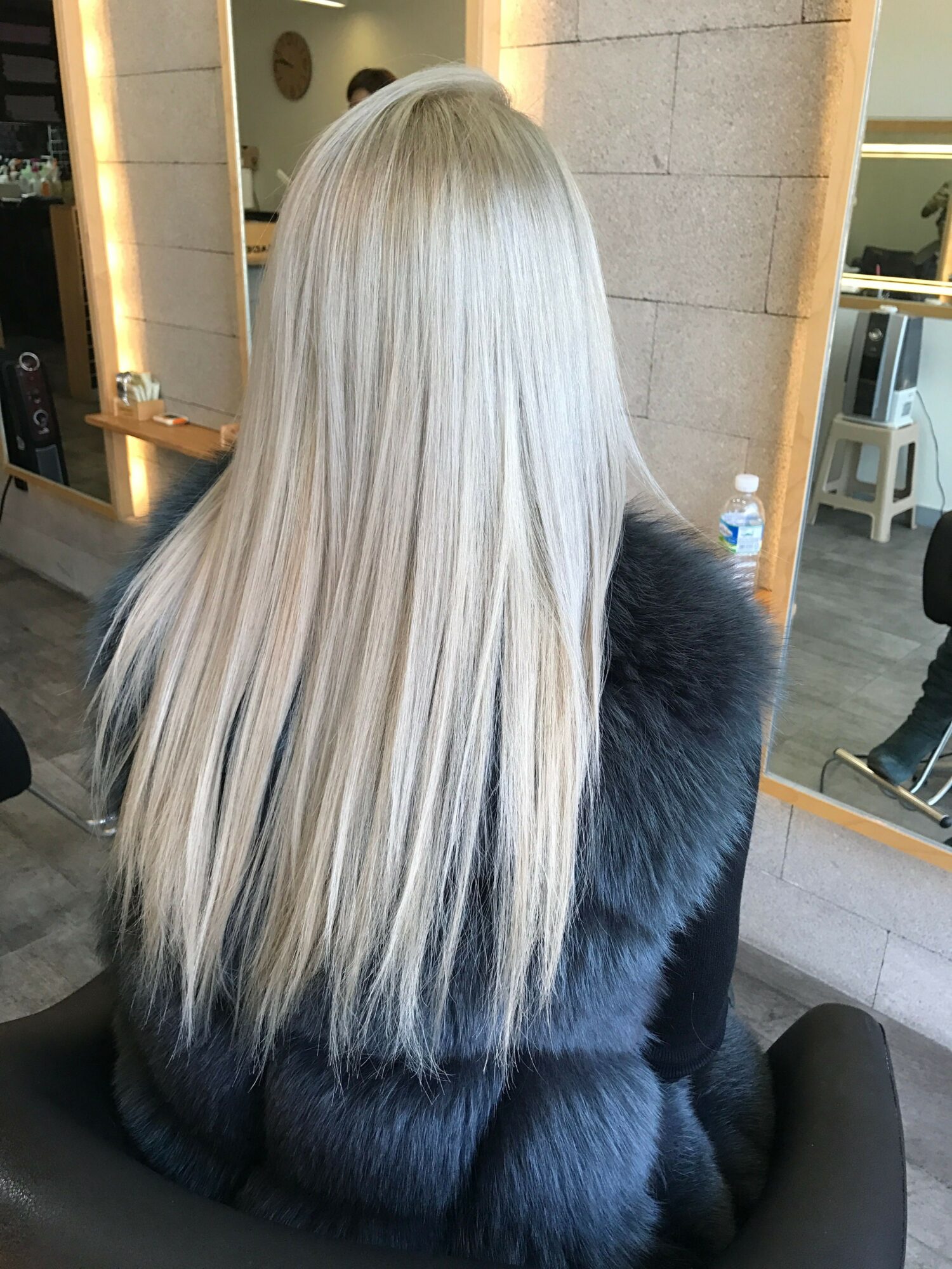 Person with long, straight, platinum blonde hair sitting in a salon chair, facing away from the camera.
