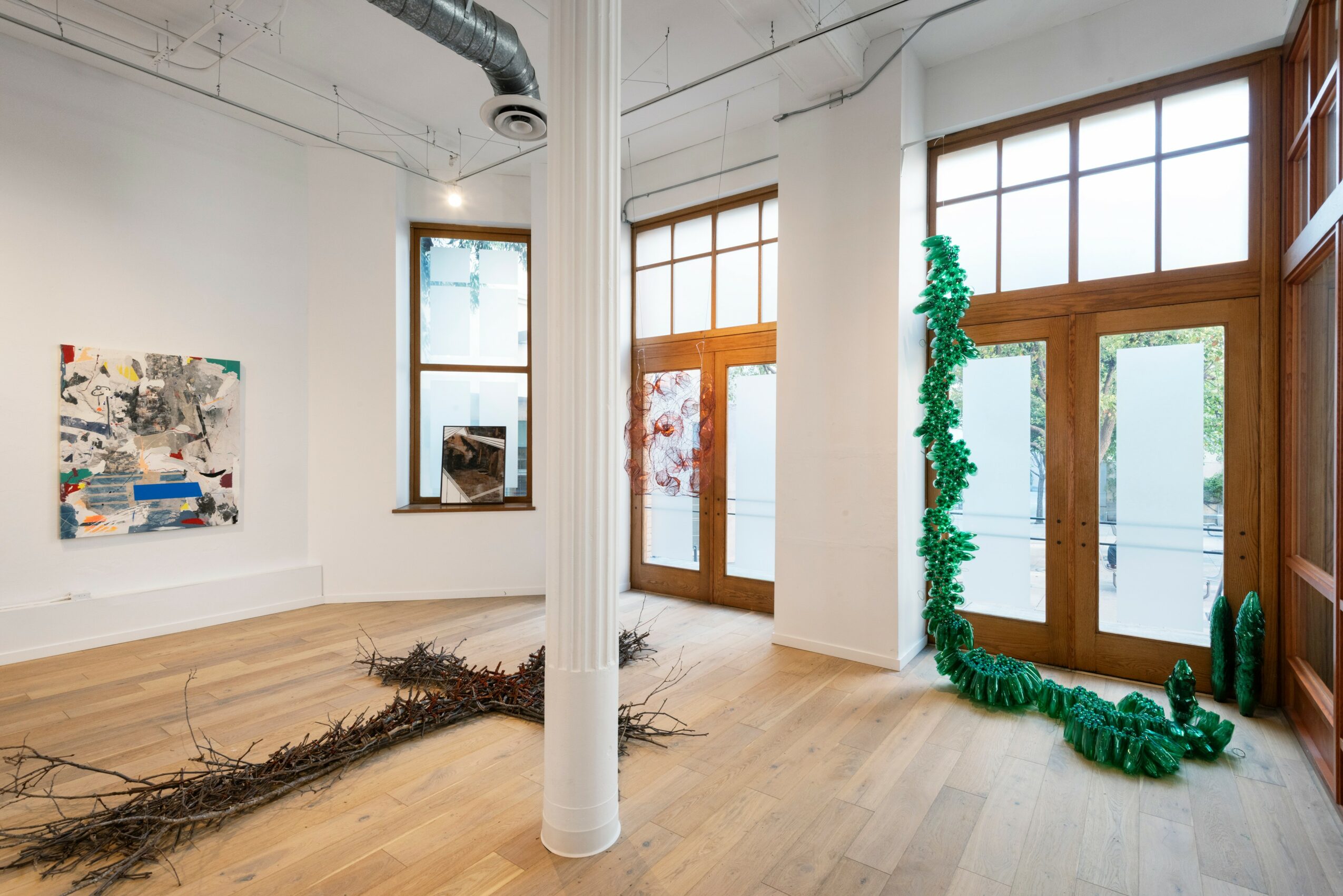 Interior space with wooden floors, large windows, white walls, and a white pillar in the center. Green decorative plant near window.