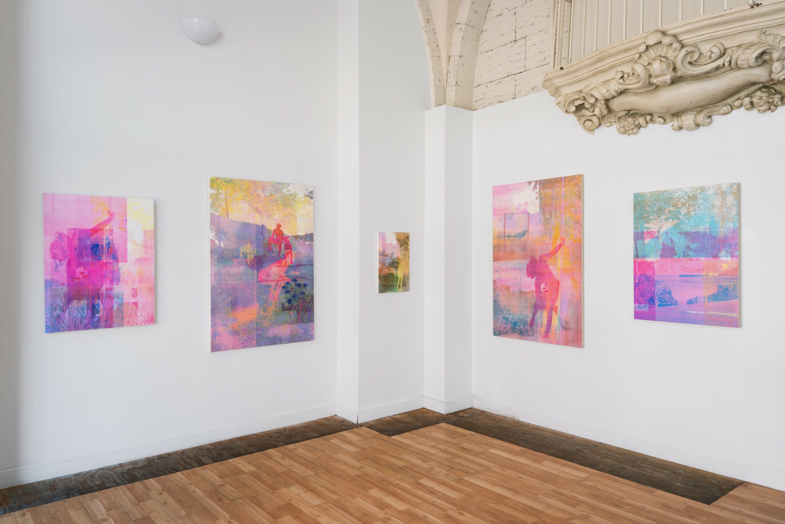 Gallery with five colorful abstract paintings on white walls and wooden floor, corner view.