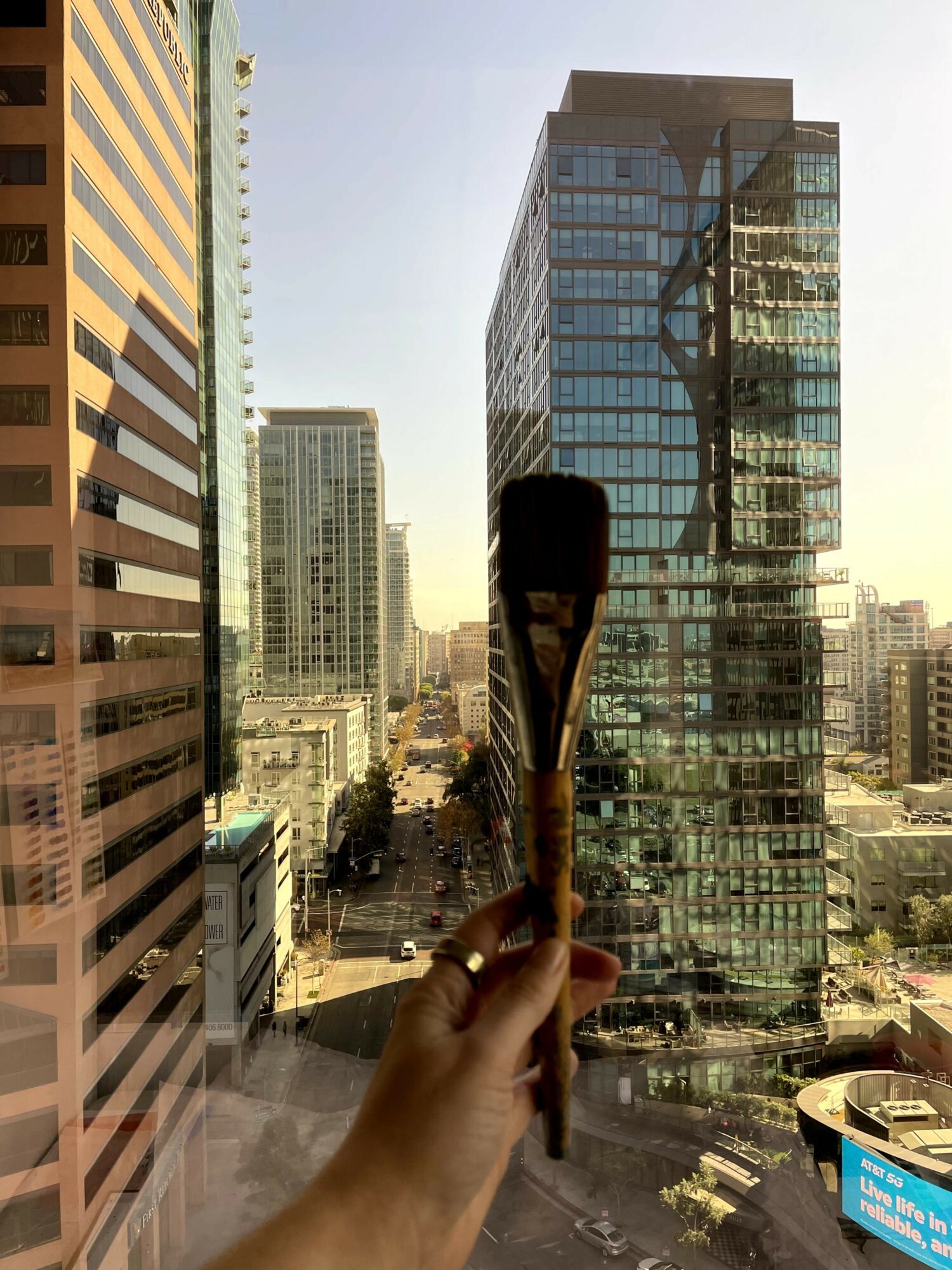 Person holding a paintbrush in front of a cityscape with tall buildings and a street below.