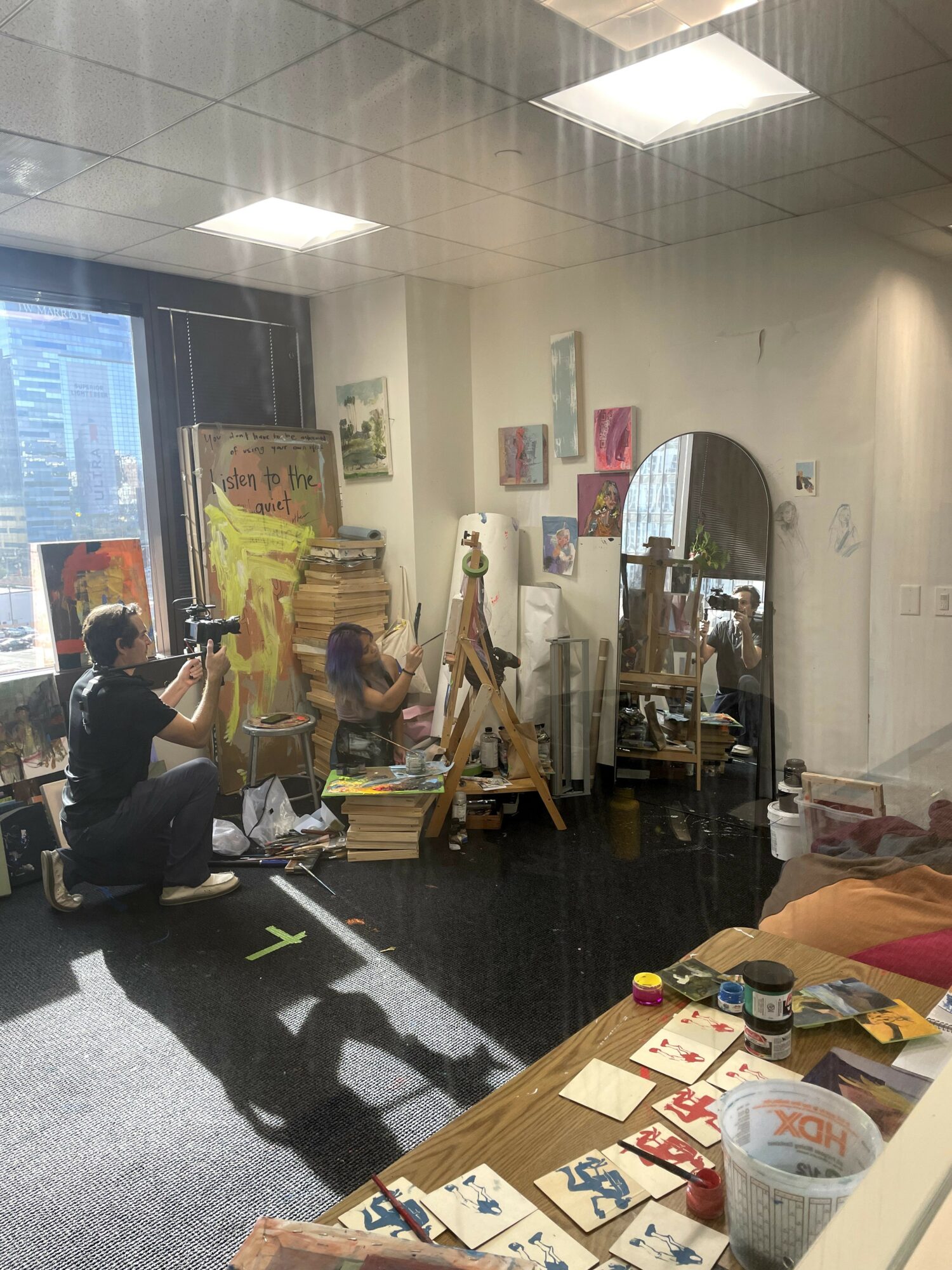 Two children painting on easels in an art studio with supplies and artwork on walls.