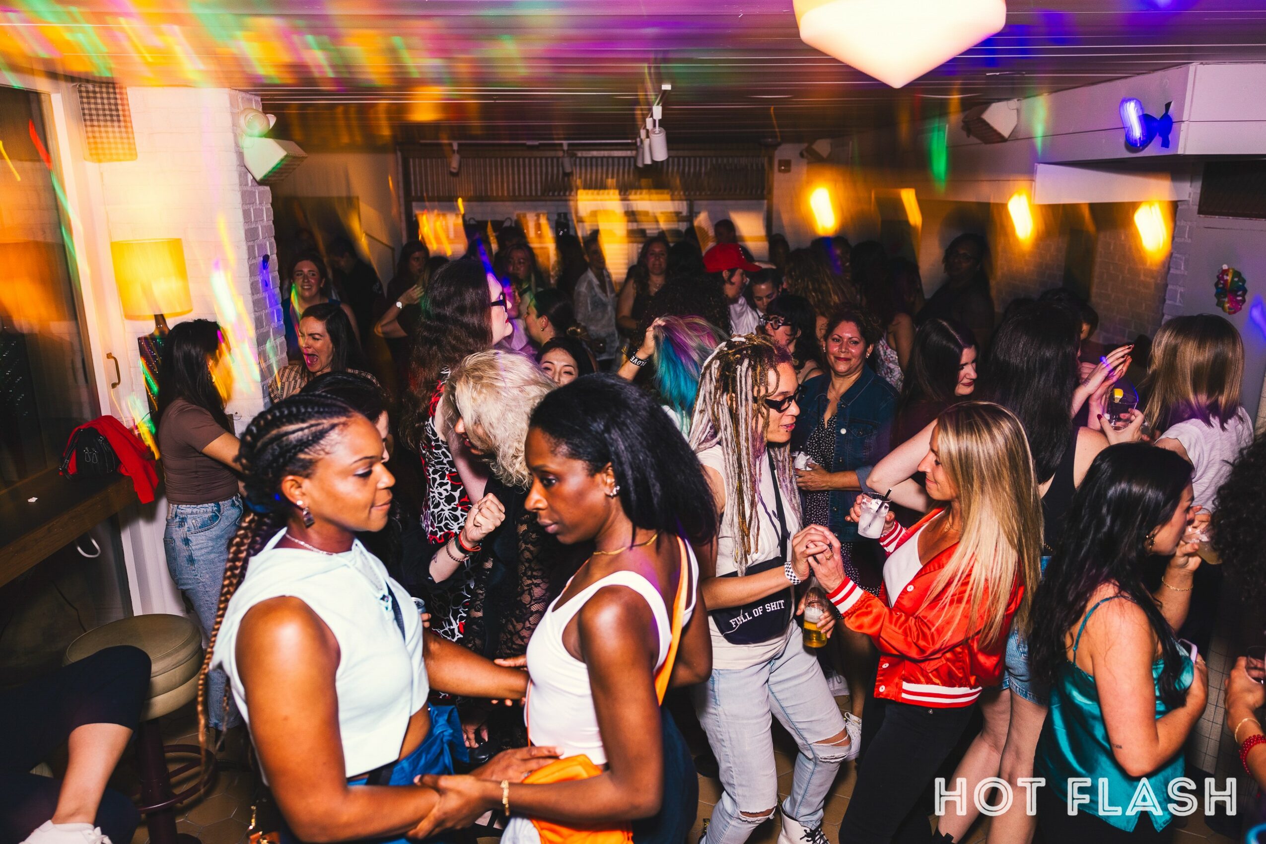 Group of people dancing and socializing in a lively indoor party setting with colorful lighting.