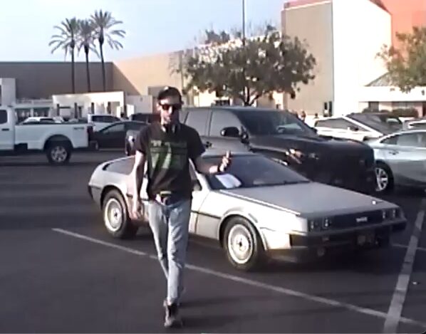 Person walking in parking lot with a vintage car and modern vehicles behind them.