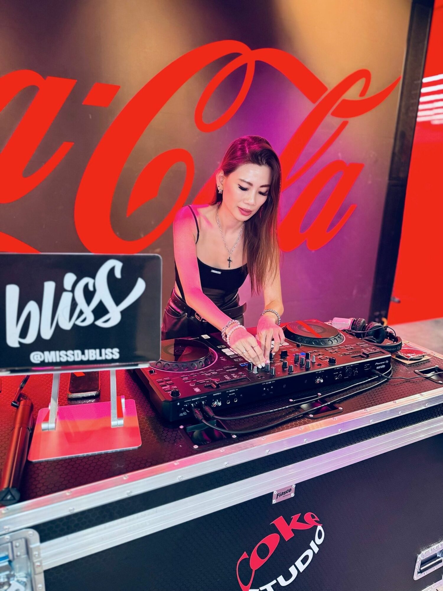 Female DJ with long hair operating DJ equipment at a studio with Coca-Cola branding.