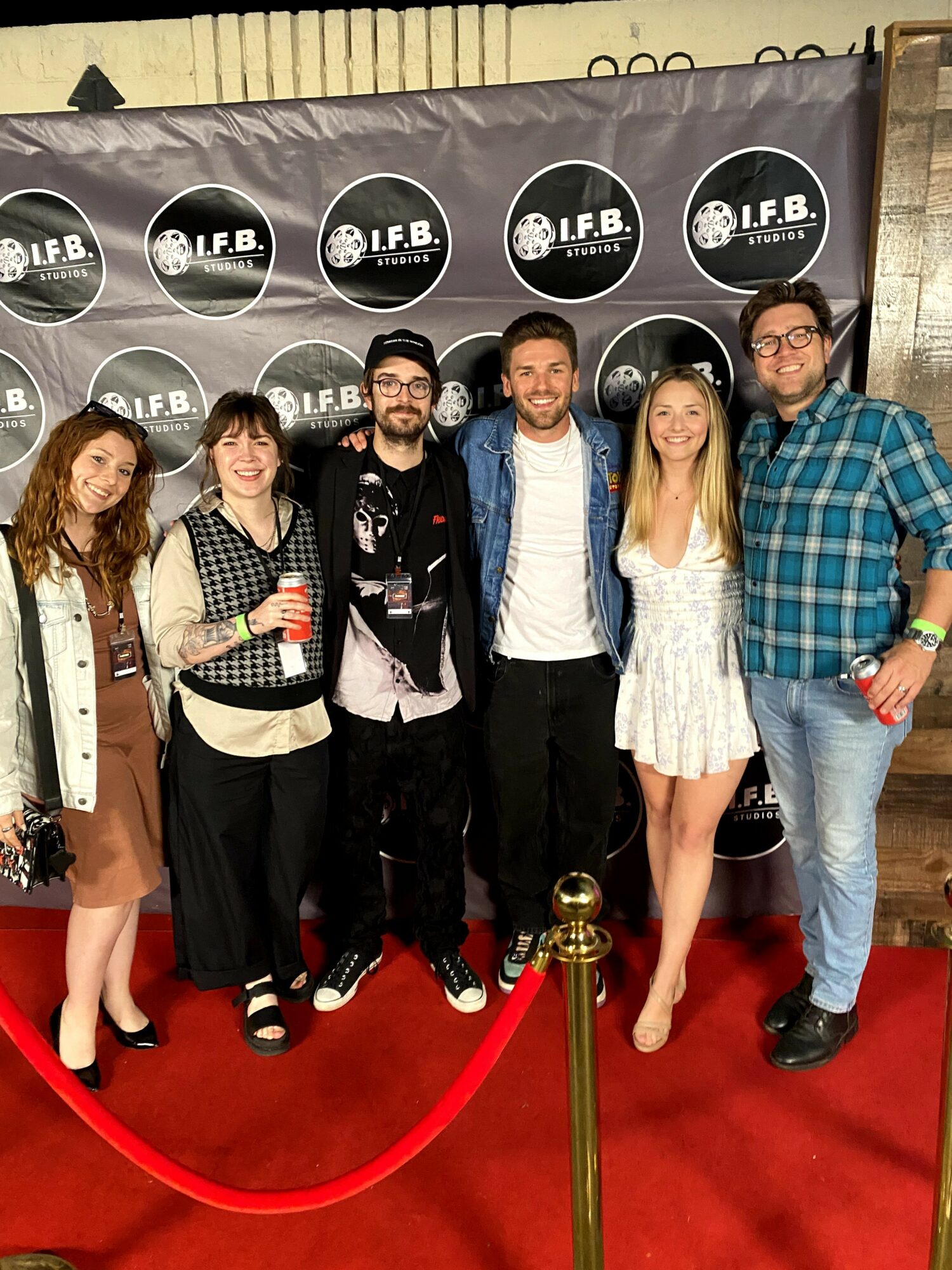 Six people standing on a red carpet in front of a black backdrop with circular logos, posing for a group photo.