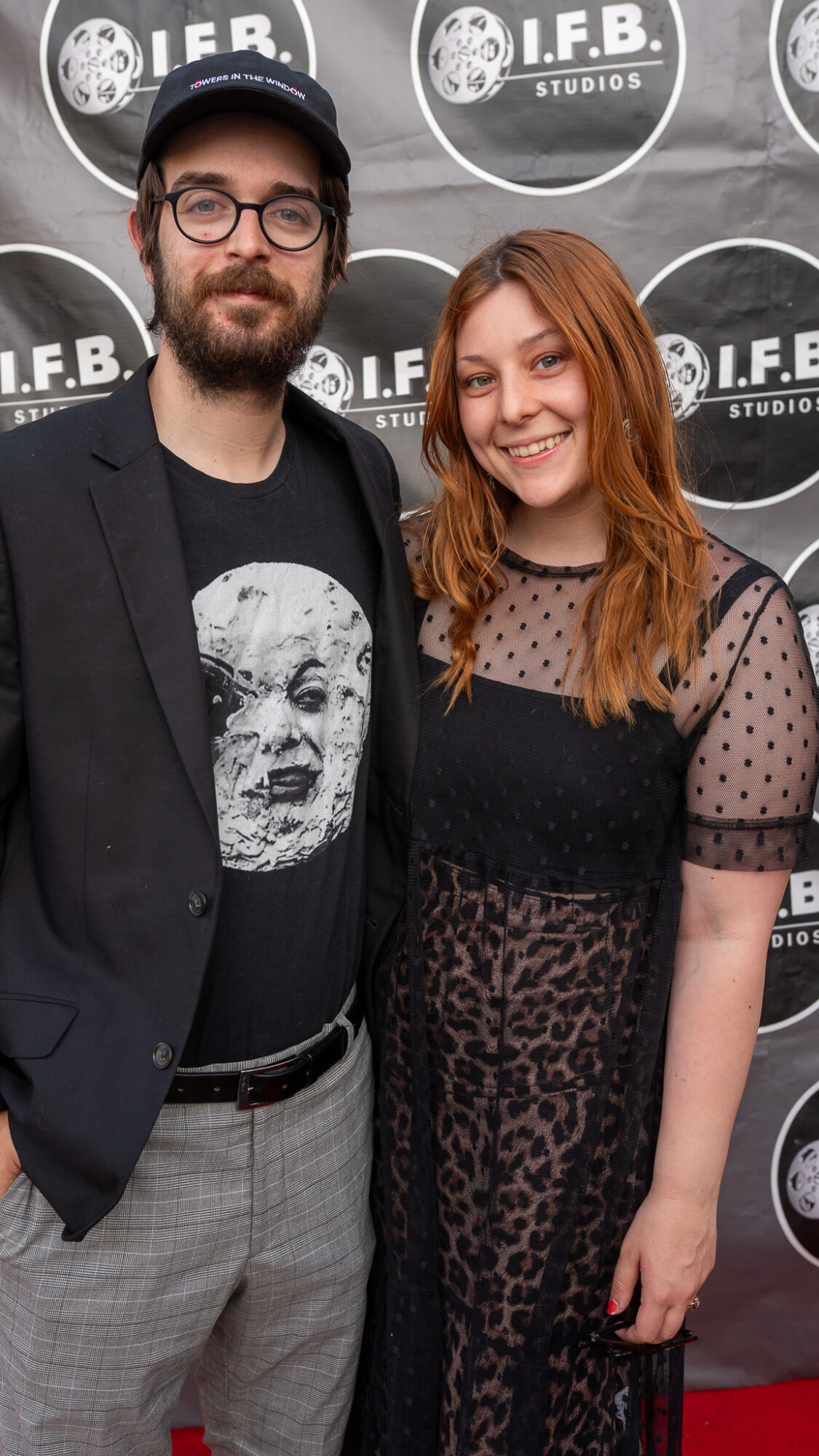 Man and woman standing together in front of a backdrop with I.F.B. Studios logo, smiling at the camera.
