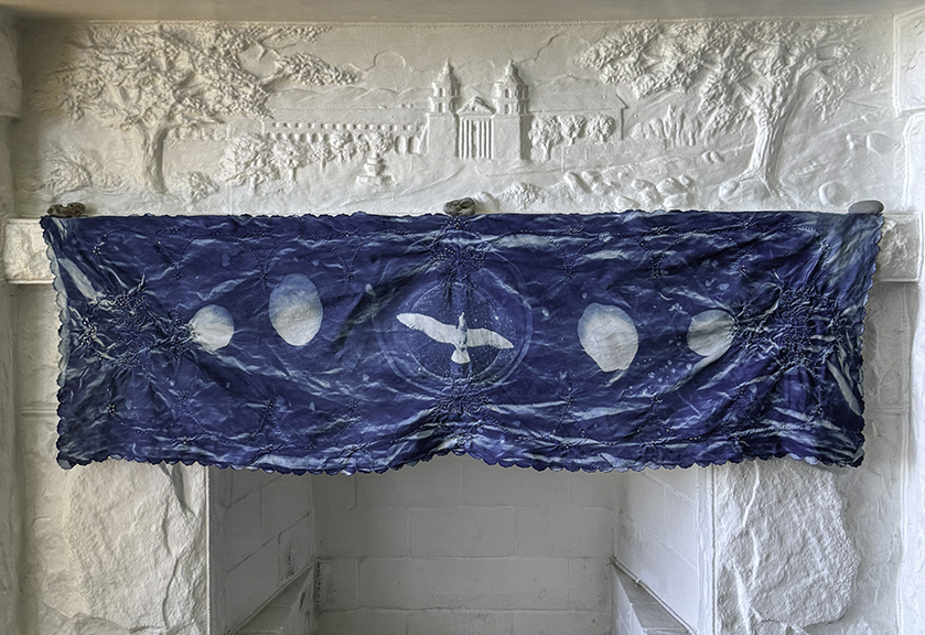 Blue fabric with white circular and bird-shaped patterns hangs on a white textured wall.