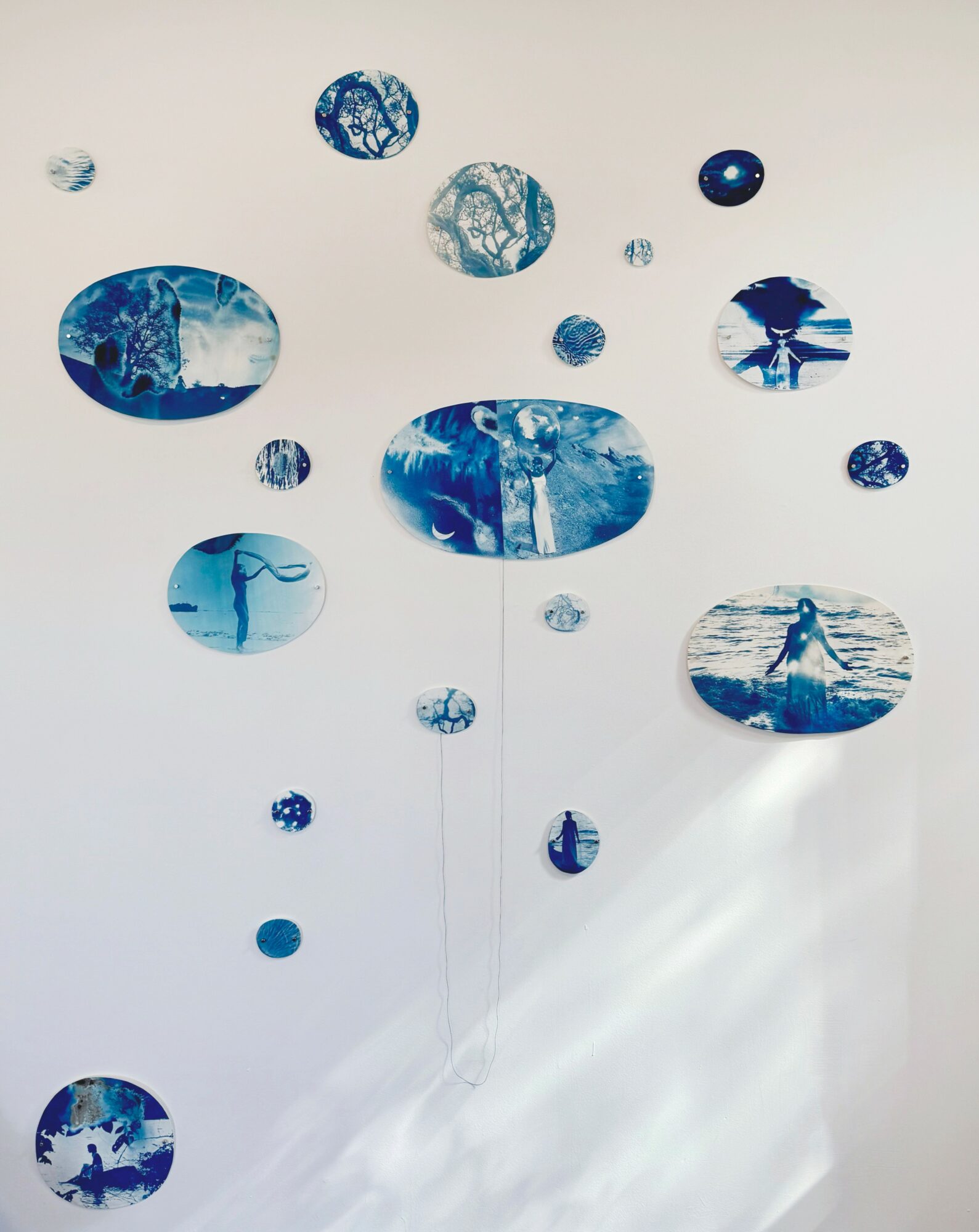 Multiple blue and white circular and oval shapes with abstract patterns hanging against a white background.