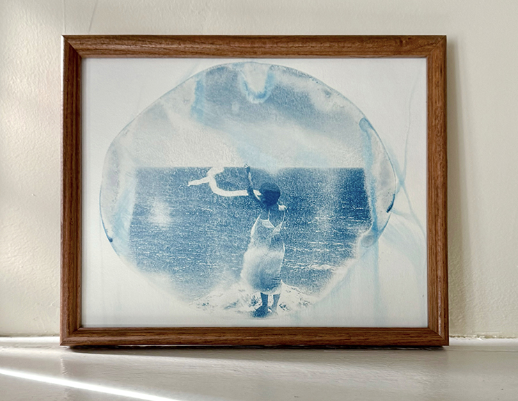 Framed watercolor painting of a person standing on a beach near water, with a cloudy sky above.
