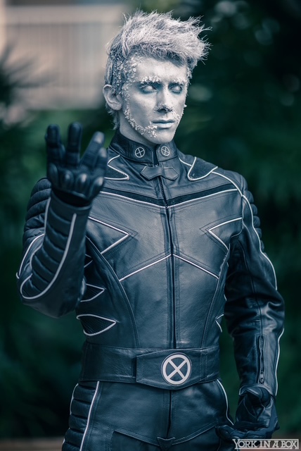 Person with short, spiky hair and metallic makeup wearing a black leather jacket outdoors.