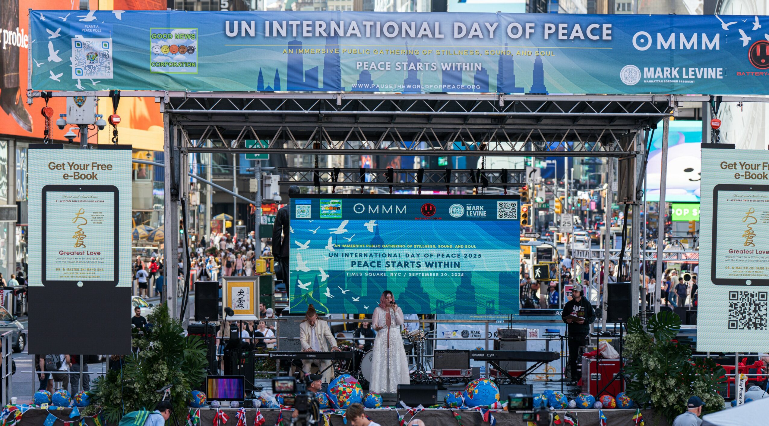 Crowd gathered in a city square for UN International Day of Peace event with banners and screens displaying peace messages.