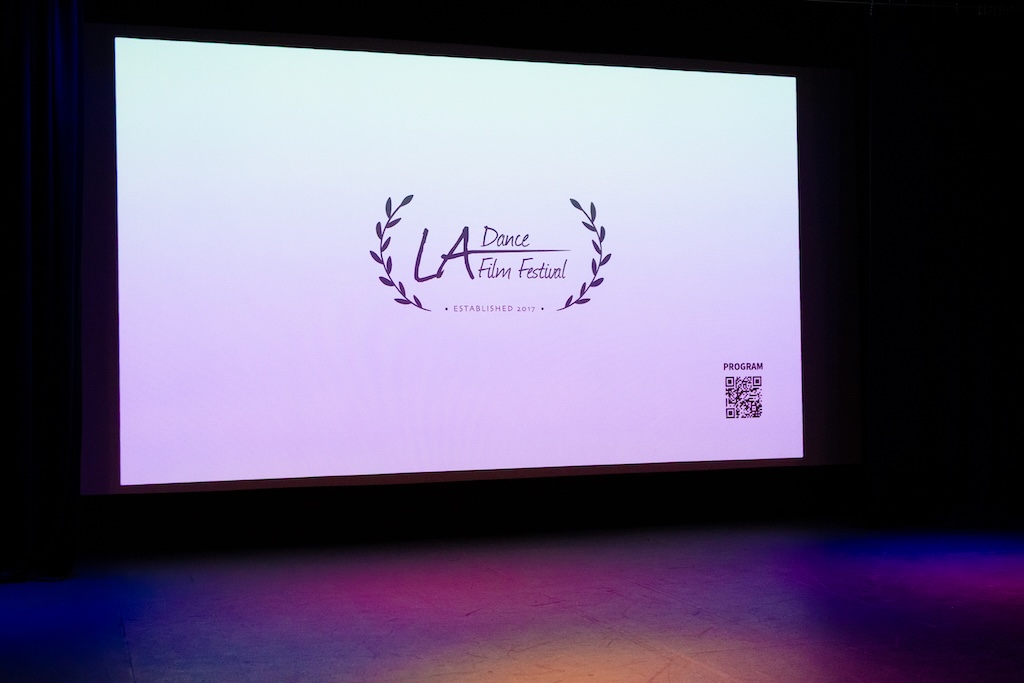 Blank screen with a logo and text for a film festival, surrounded by laurel branches, and a QR code in the bottom right corner.