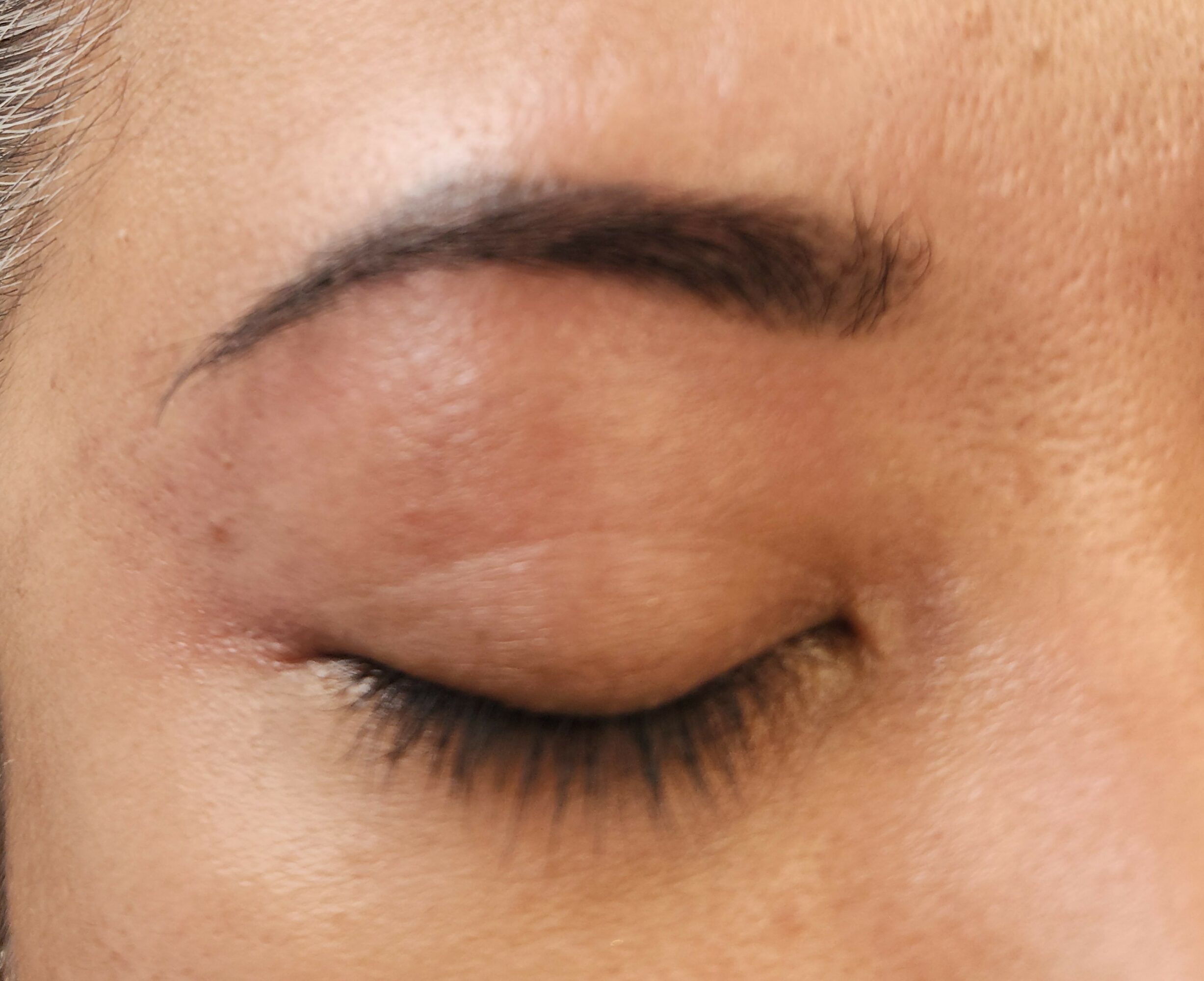 Closed eye with visible eyebrow and eyelashes, skin with slight texture and natural tone.