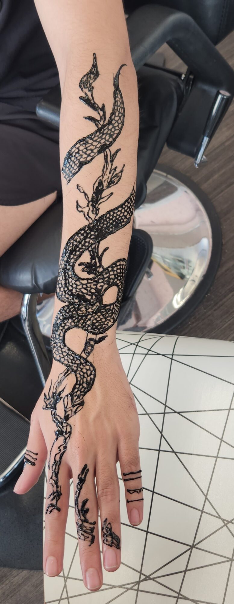 Black and gray snake tattoo on person's forearm and hand, with scales and detailed features.