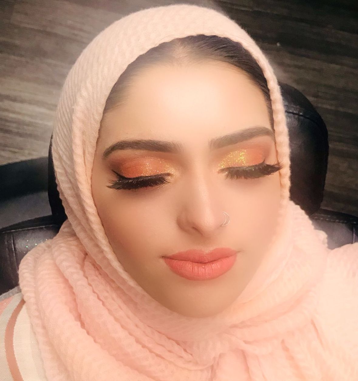 Close-up of a woman with makeup and a pink headscarf, eyes closed, smiling softly.