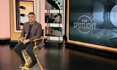 Man sitting on a director's chair in a television studio with cameras and screens around him.