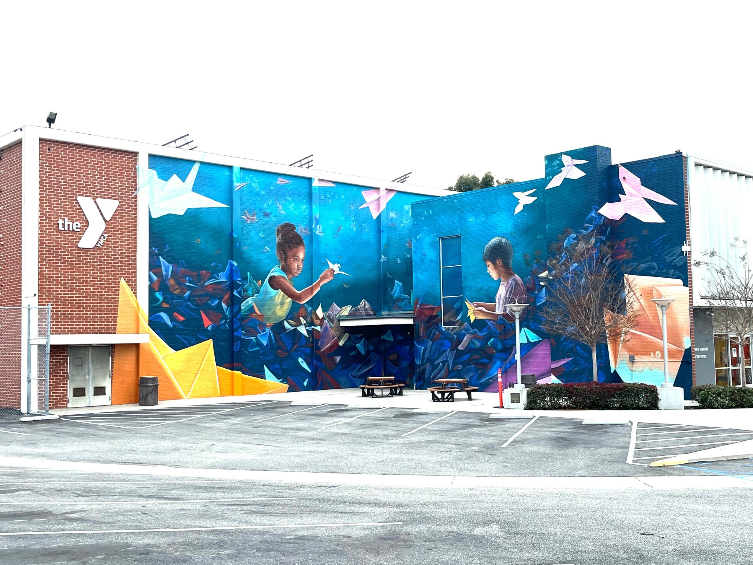 Colorful mural on building wall depicts children playing musical instruments outdoors with trees and abstract shapes.