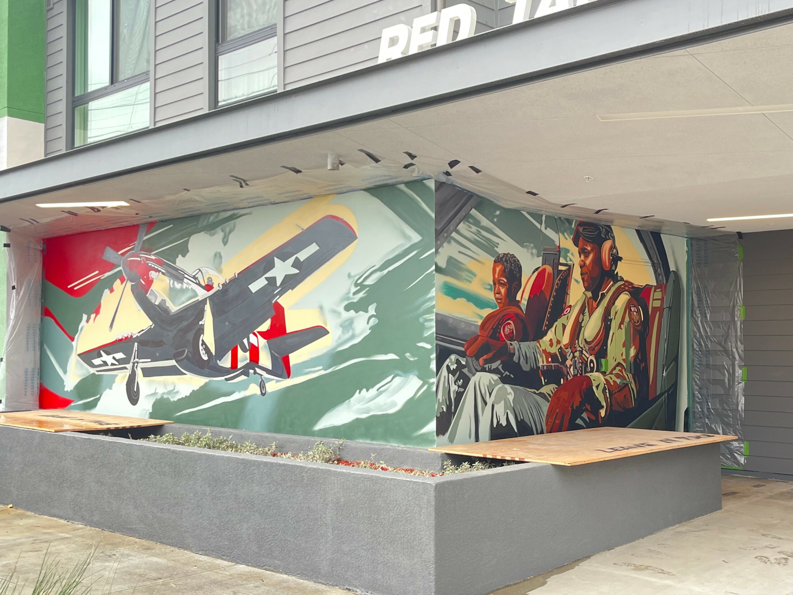 Colorful mural of a vintage airplane and two people sitting, painted on a building wall.
