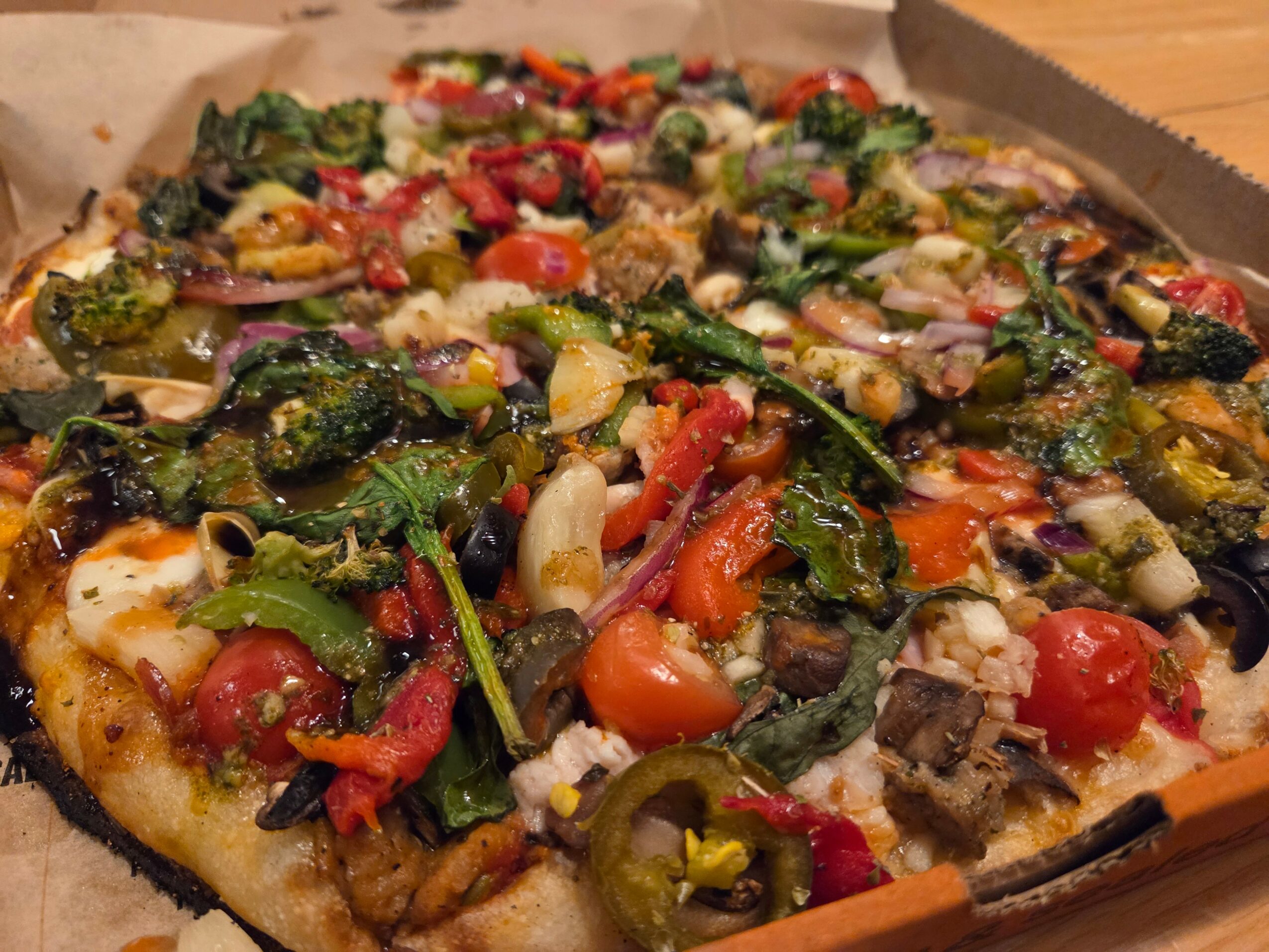 Pizza topped with cherry tomatoes, green peppers, onions, olives, and leafy greens.