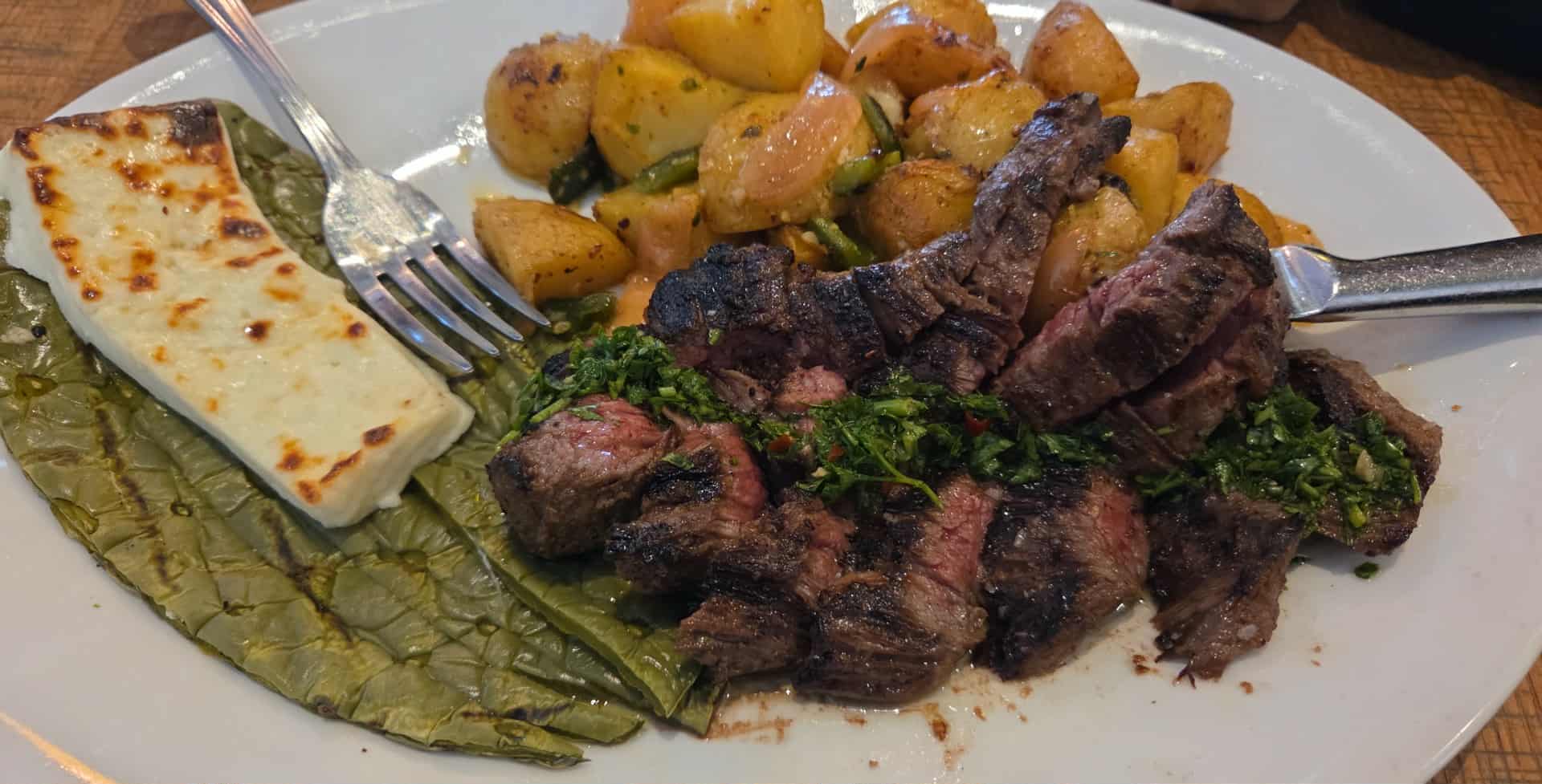Plate with grilled meat, roasted potatoes, grilled cheese, and a leaf of lettuce.