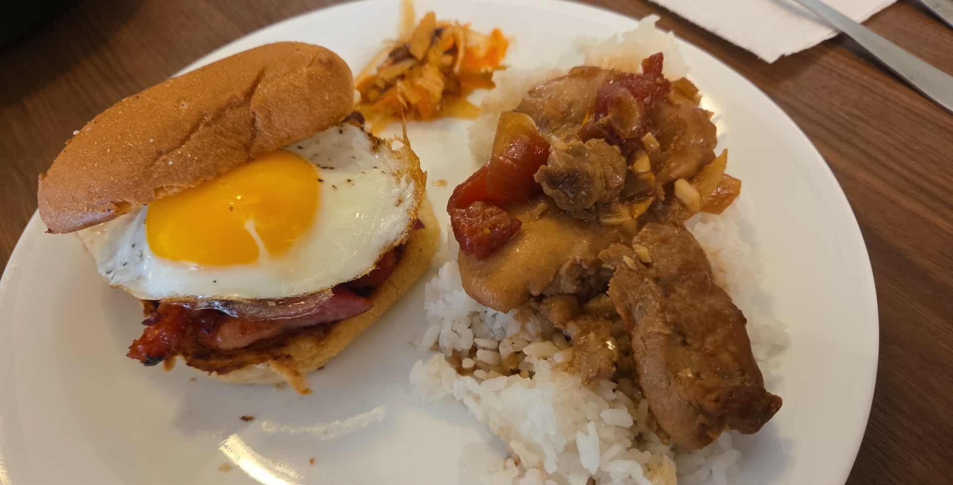 Plate with fried egg sandwich, rice, and vegetable stew, on a wooden table.