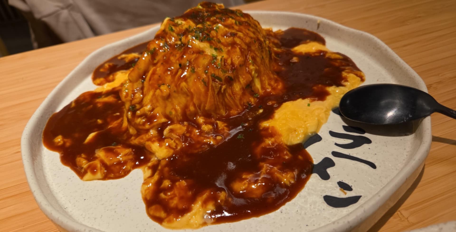 Dish with rice, topped with a large portion of meat covered in dark sauce, served on a white tray with a spoon.