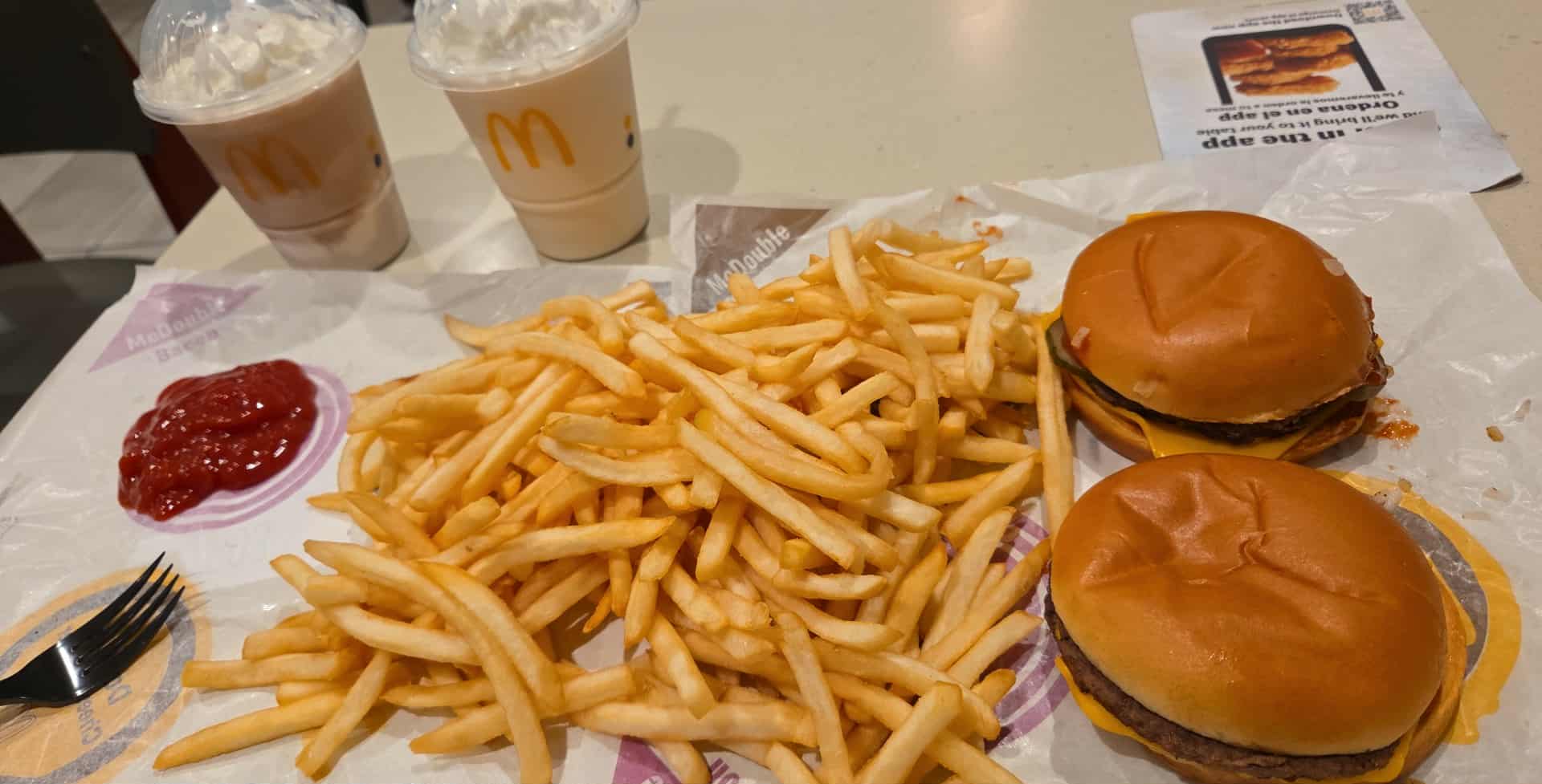 Two burgers, a large pile of French fries, two drinks, and ketchup on a tray.