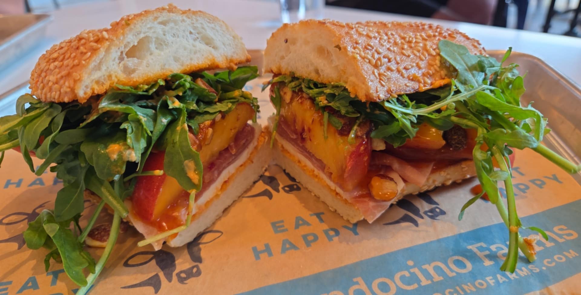 Two sandwiches with lettuce, tomato, bacon, and other ingredients on a tray with paper lining.