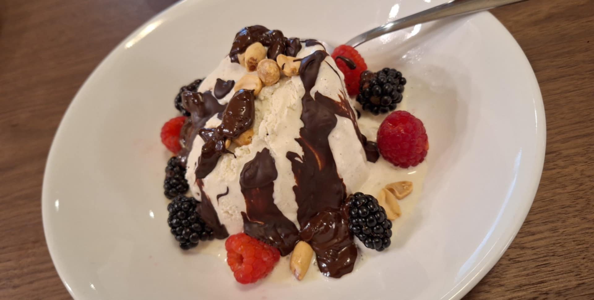 Dessert with whipped cream, berries, chocolate drizzle, and nuts on a white plate.