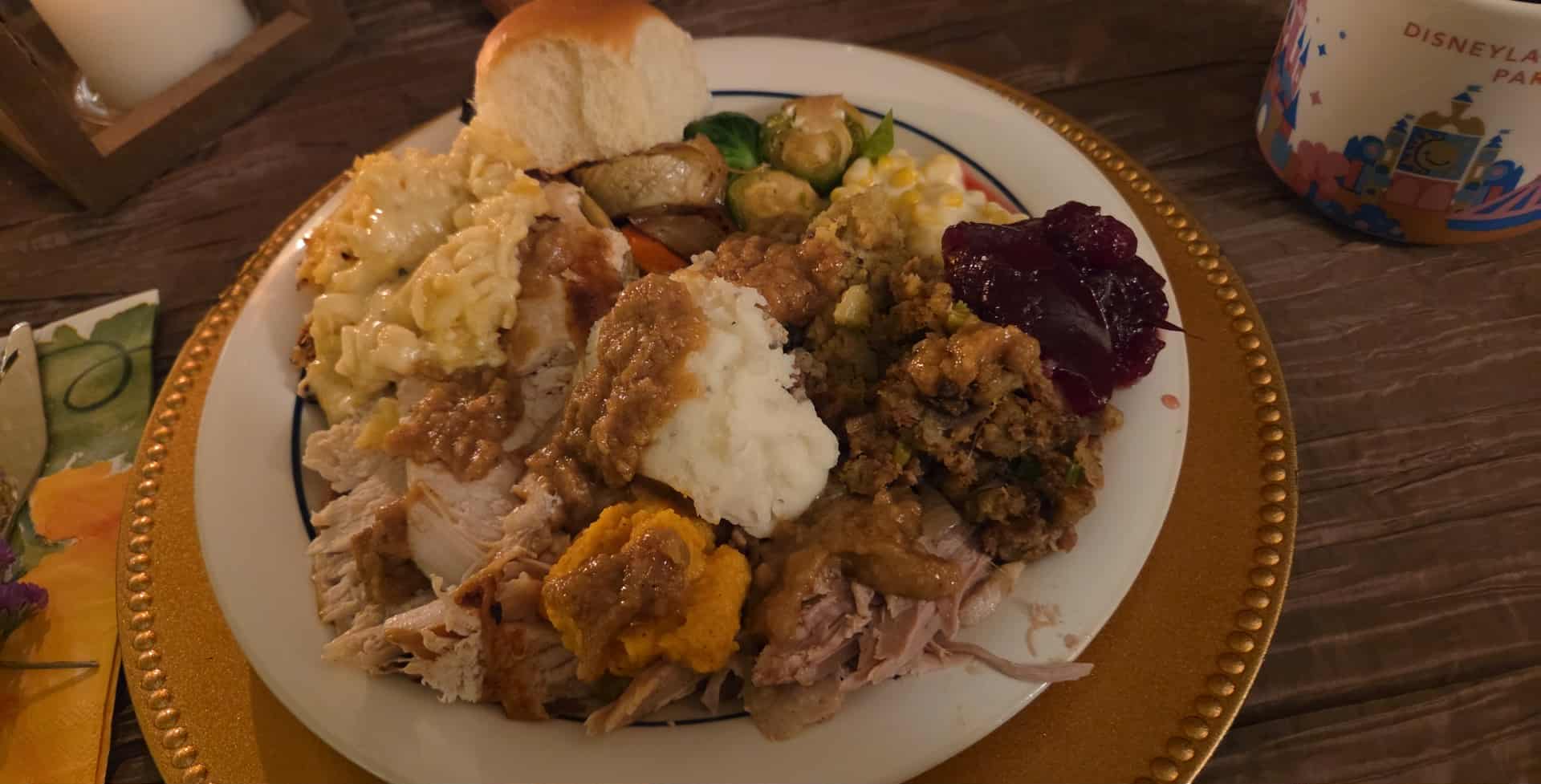 Plate with mashed potatoes, turkey, stuffing, cranberry sauce, bread, and vegetables on a wooden table.