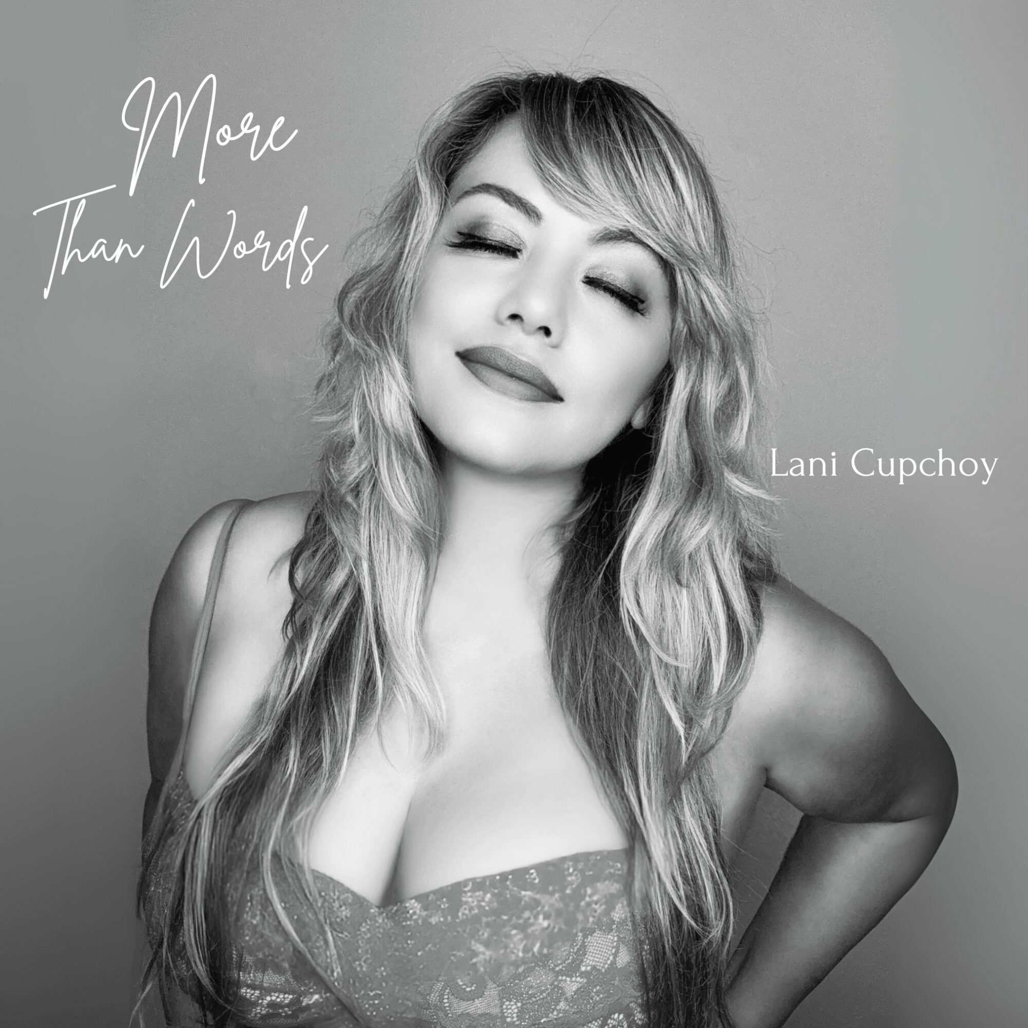 Woman with wavy hair smiling with eyes closed, wearing a patterned top, against a plain background.