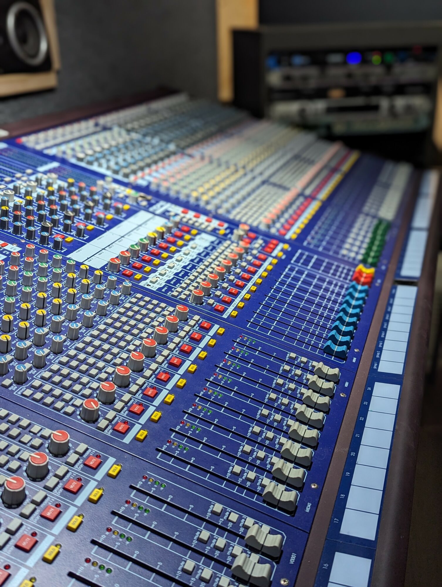 Audio mixing console with numerous sliders, knobs, and buttons in a recording studio.