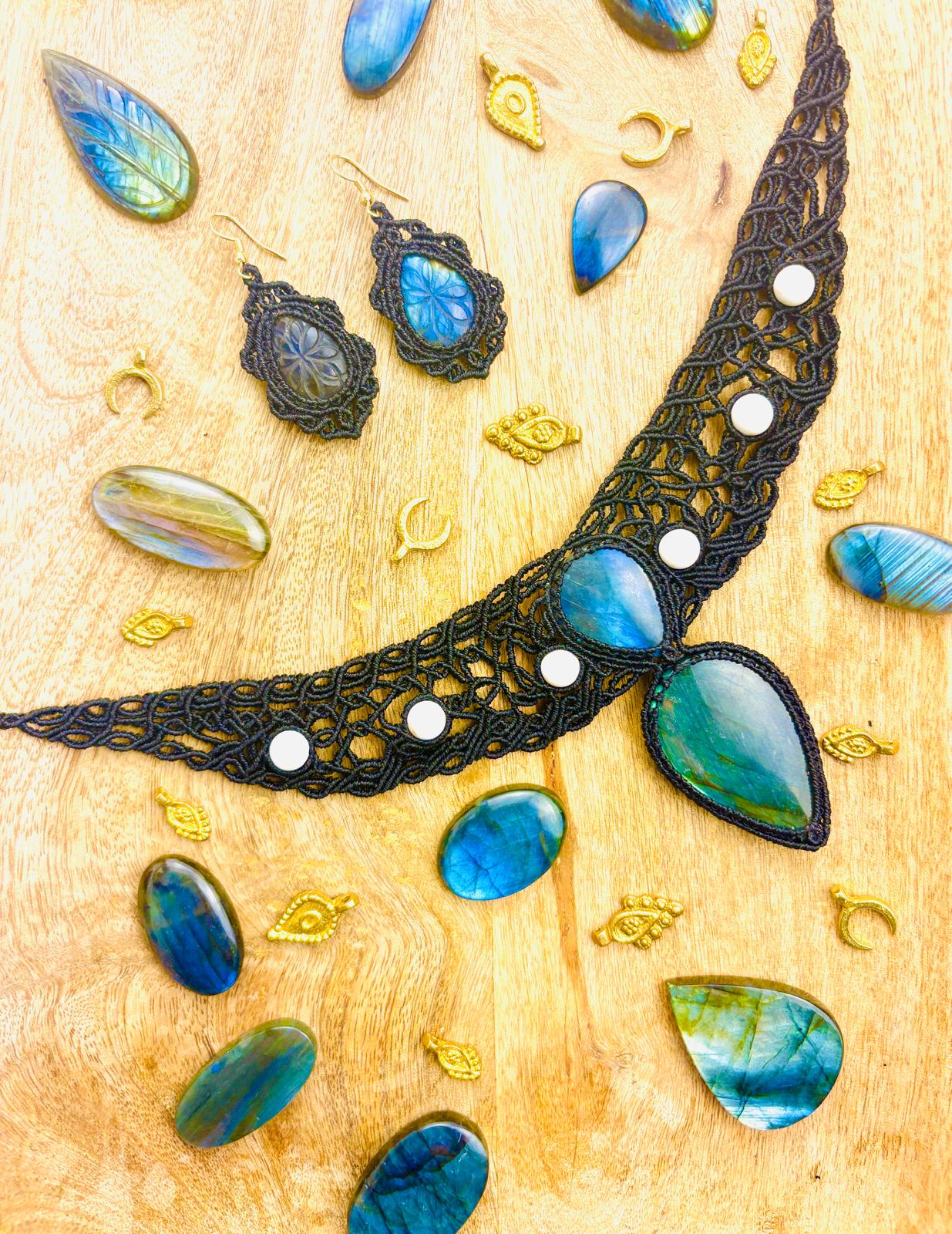 Jewelry pieces including a large black lace necklace with blue stones, matching earrings, and scattered blue and gold decorative elements on a wooden surface.