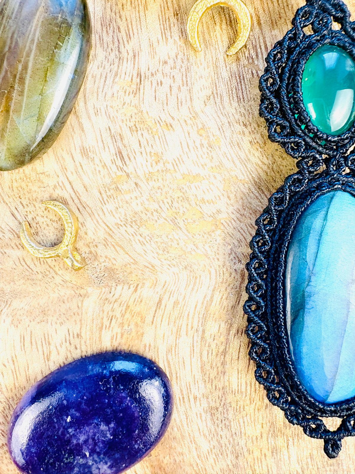 Various gemstones and jewelry pieces on a wooden surface, including a large blue stone and a black lace pendant.