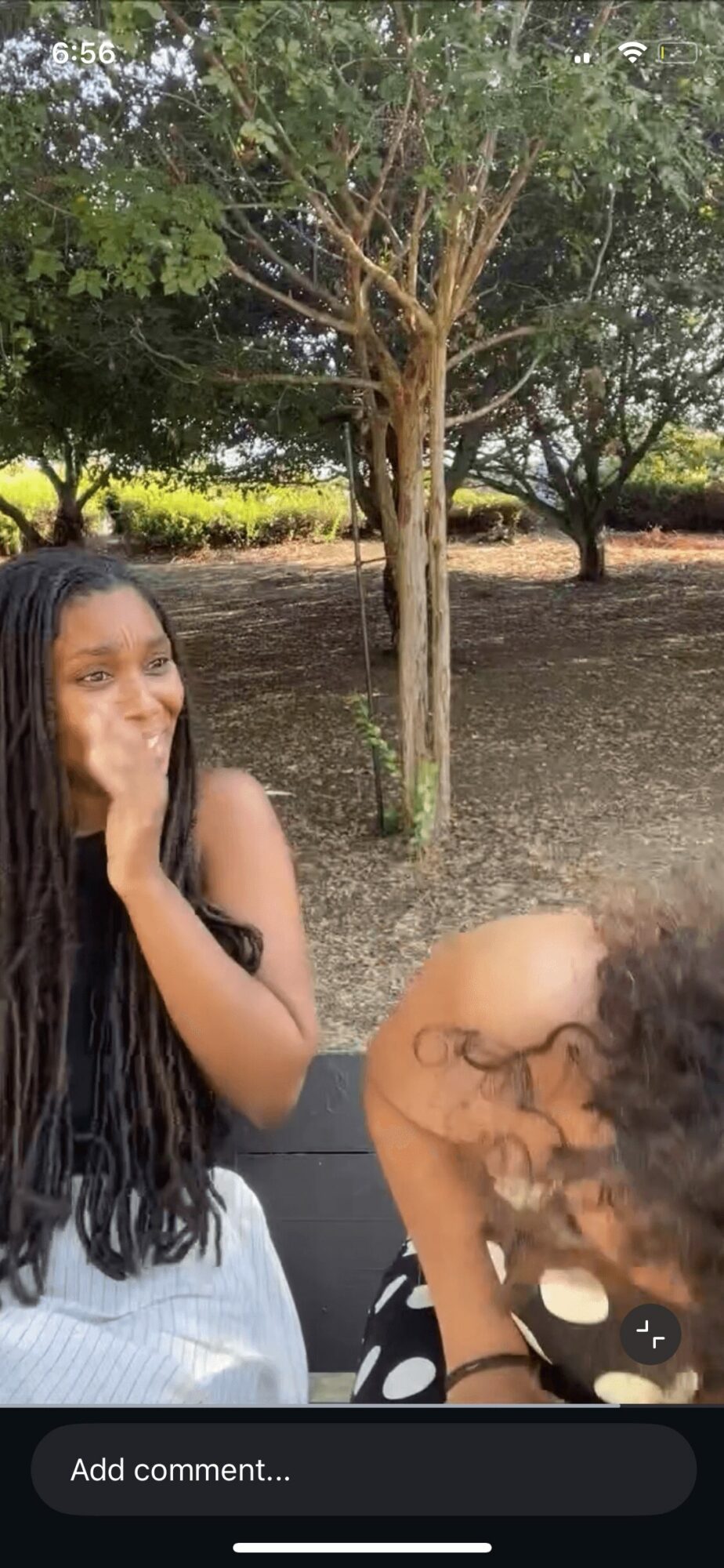 Two children outdoors near a tree, one with long dark hair and the other with curly hair, both smiling.