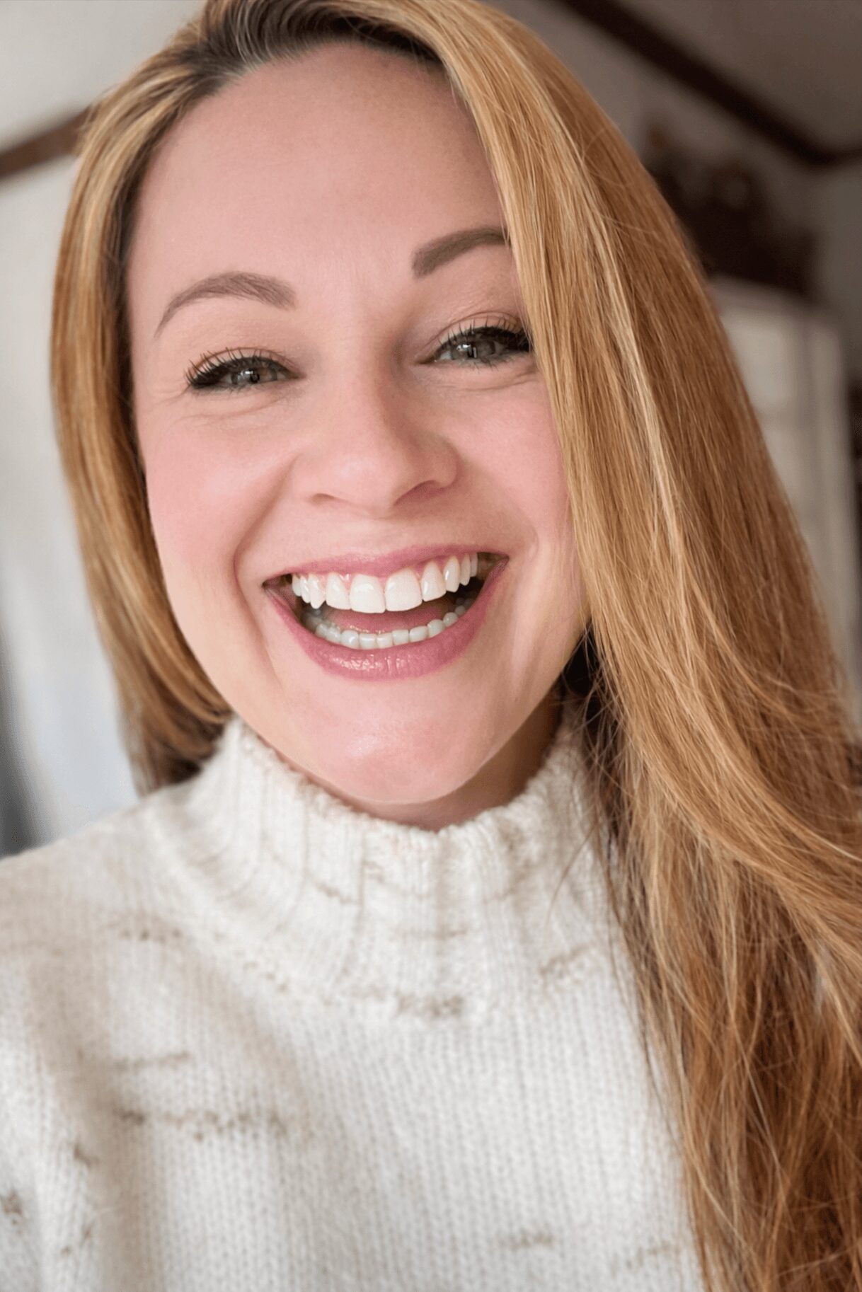 Close-up of smiling woman with long, light brown hair wearing a white turtleneck sweater.