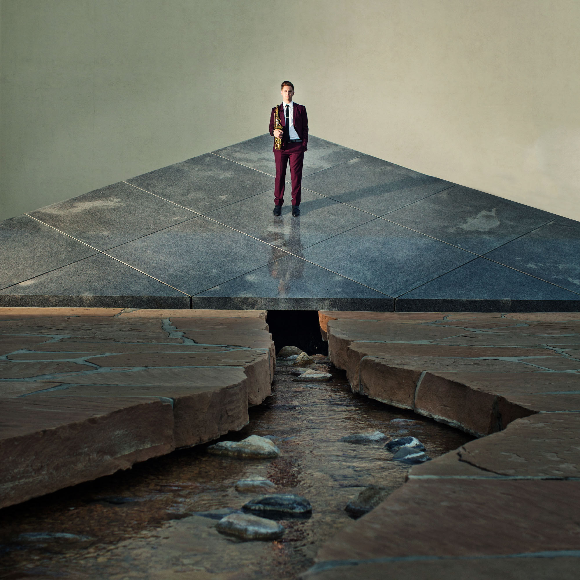 Person standing on a raised platform above a rocky stream, with a plain background.