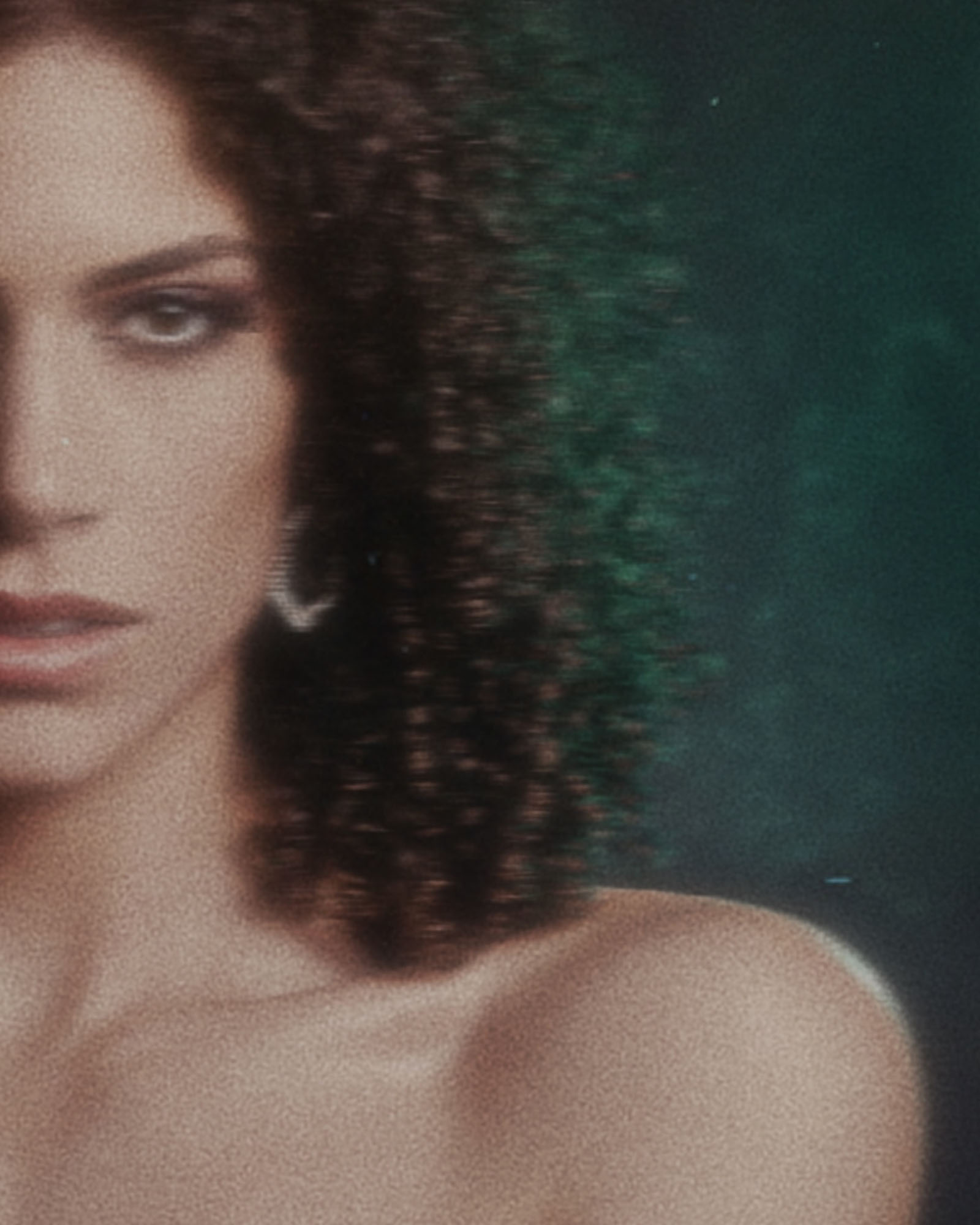 Close-up of a woman with curly hair and earrings, partially visible face, and shoulder.