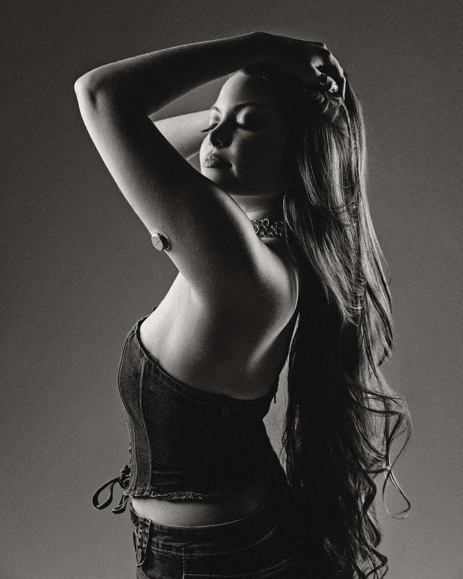 Woman with long hair poses with arm raised, eyes closed, in black and white photo.