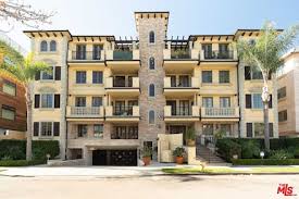 Multi-story residential building with balconies, central tower, and palm trees in front, under clear sky.