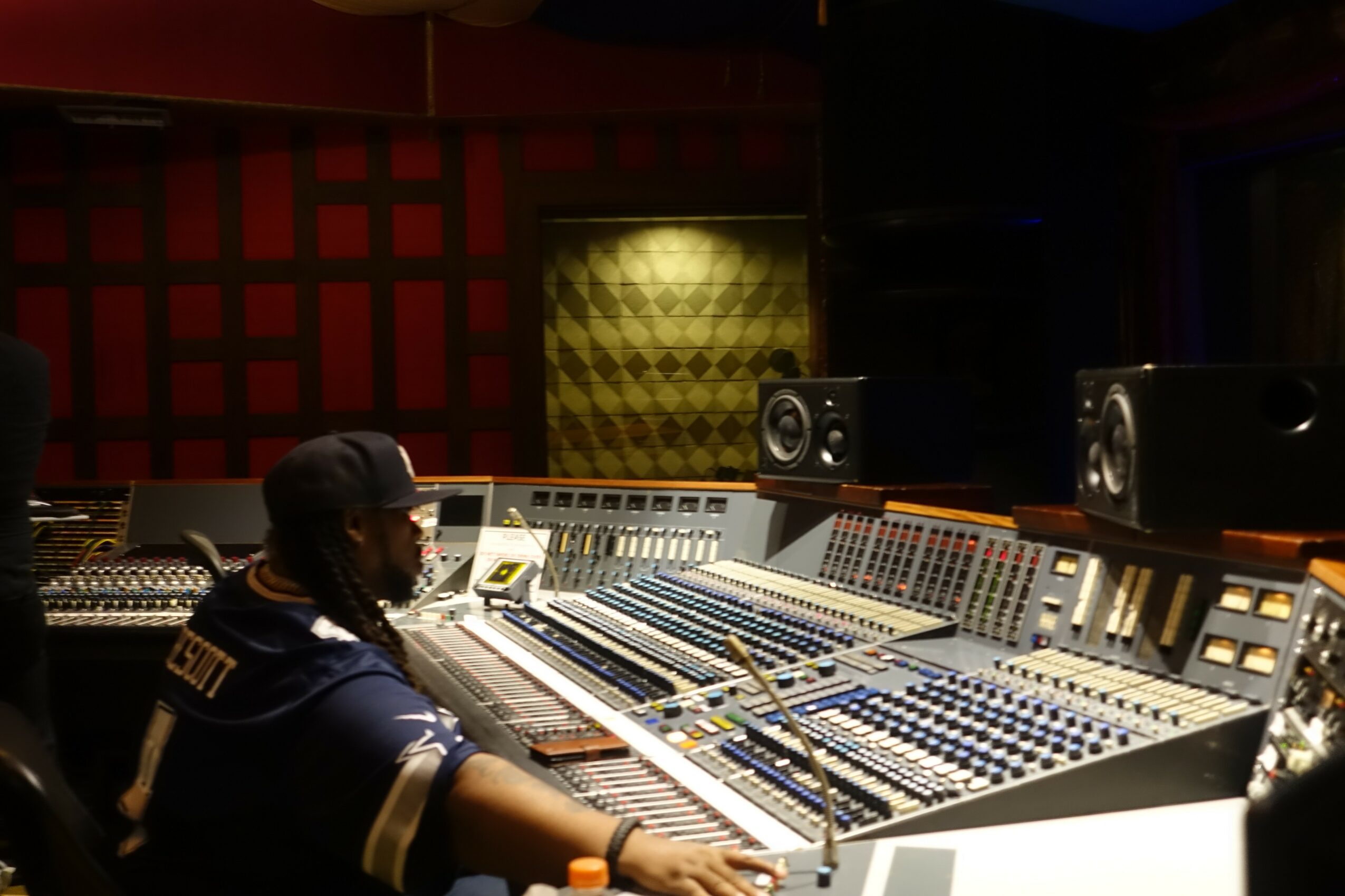 Person wearing headphones and a cap working at a large audio mixing console in a recording studio.