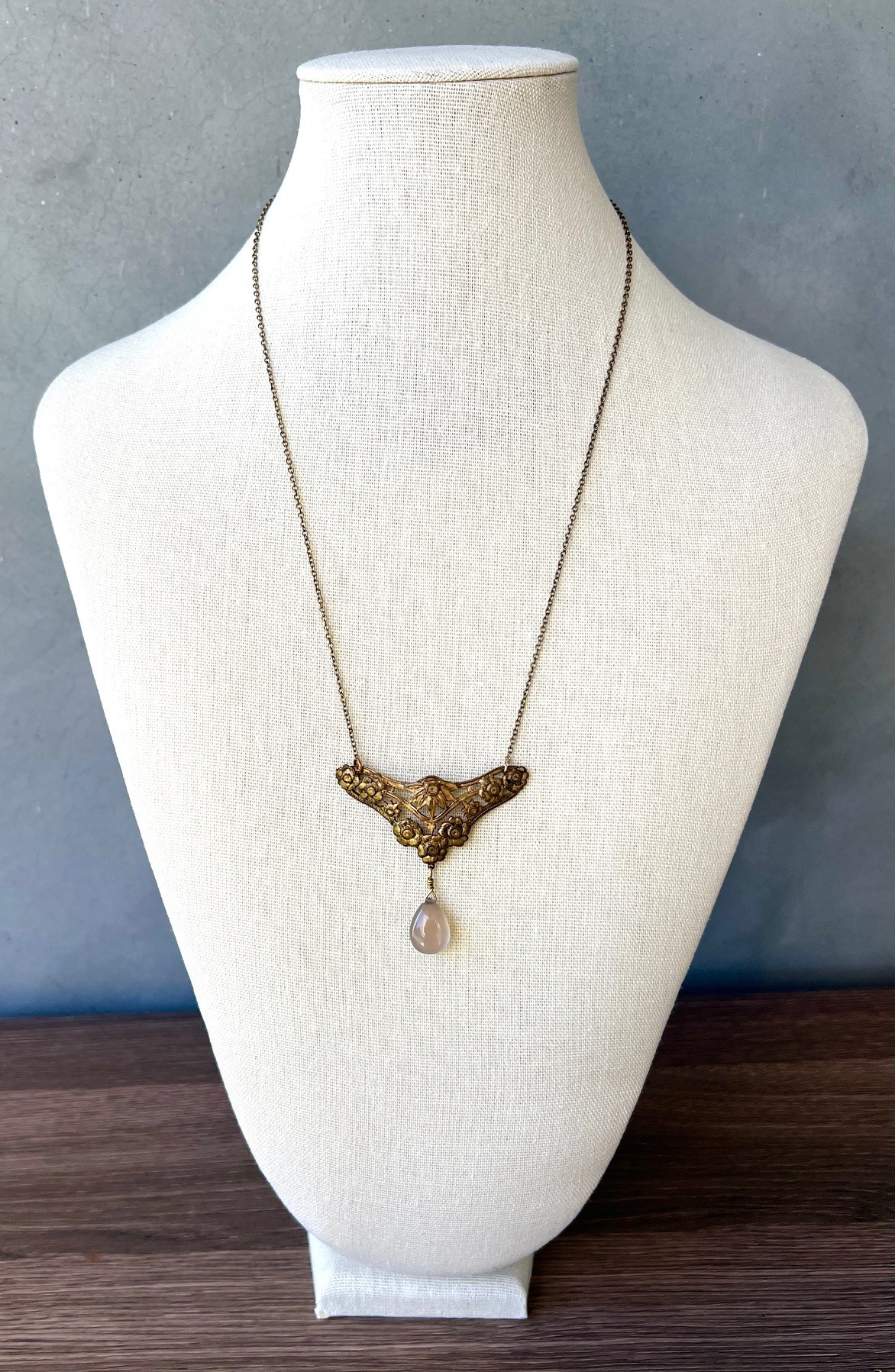 Necklace with a bird-shaped pendant and a teardrop-shaped charm displayed on a white bust.