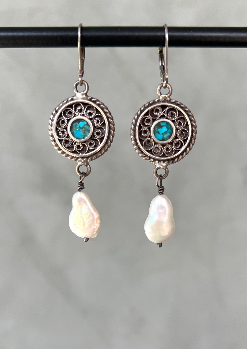 Silver earrings with intricate circular design, blue gemstone center, and dangling white pearl drops.