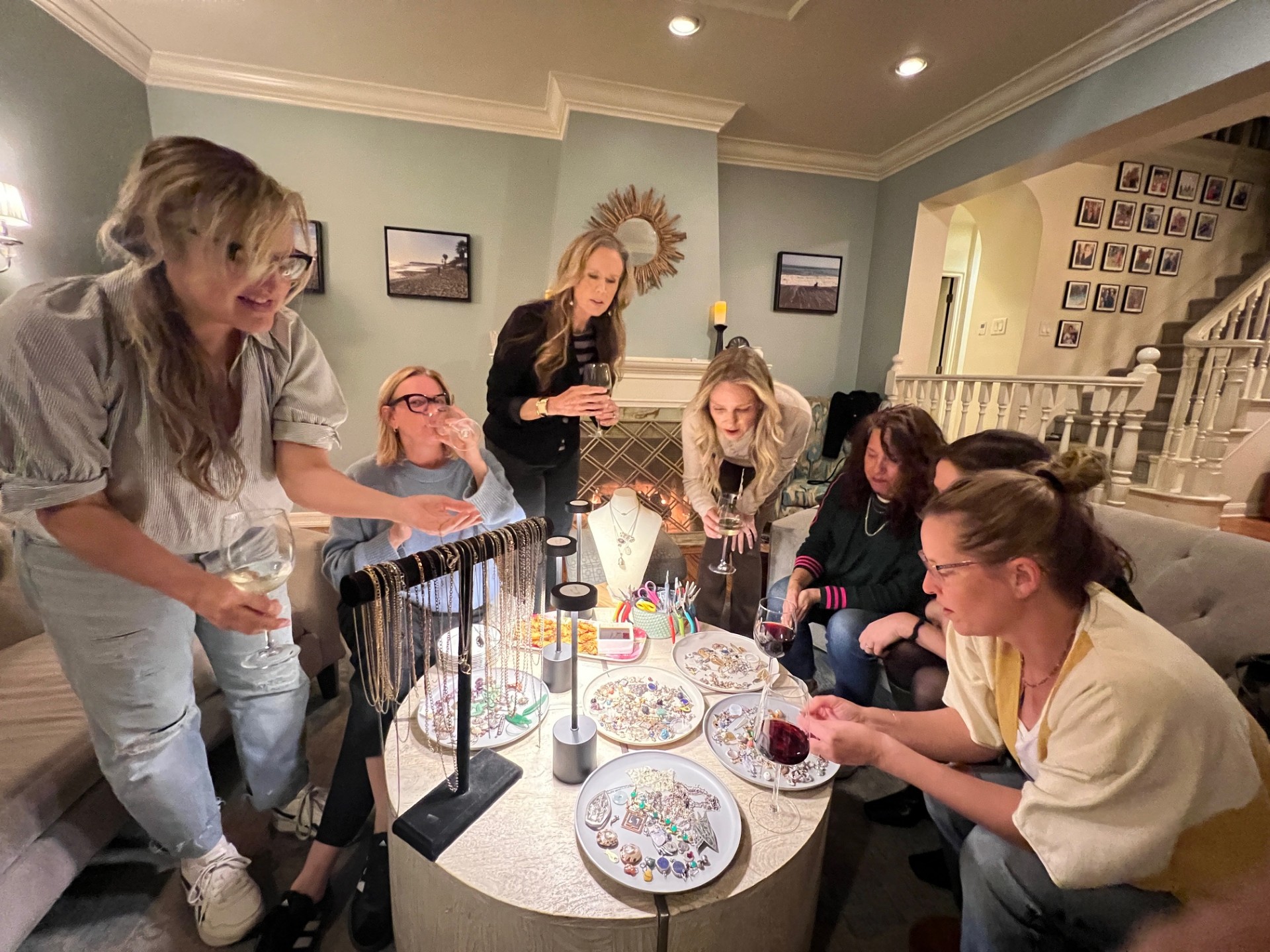 Group of women gathered around a table with jewelry and decorative items, engaging in conversation and examining objects.