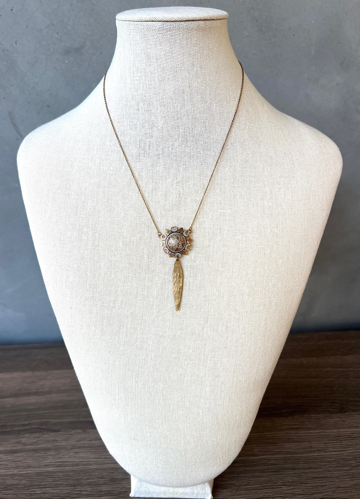 Necklace with a round pendant and a feather charm displayed on a white mannequin bust.