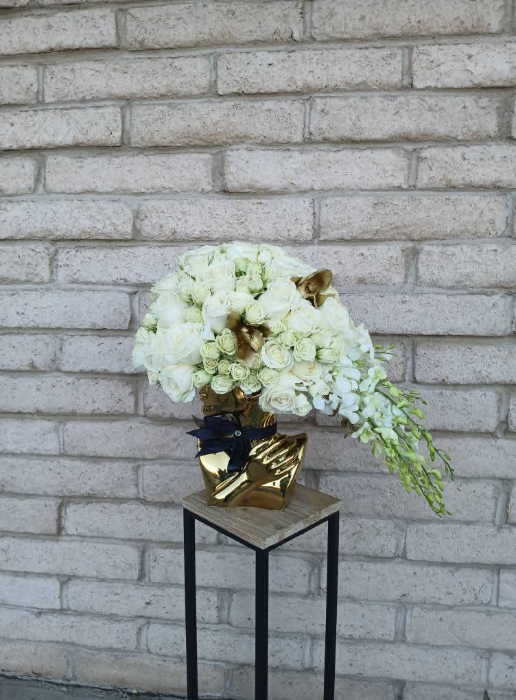 Flower arrangement with white blooms and greenery on a small table against a brick wall.