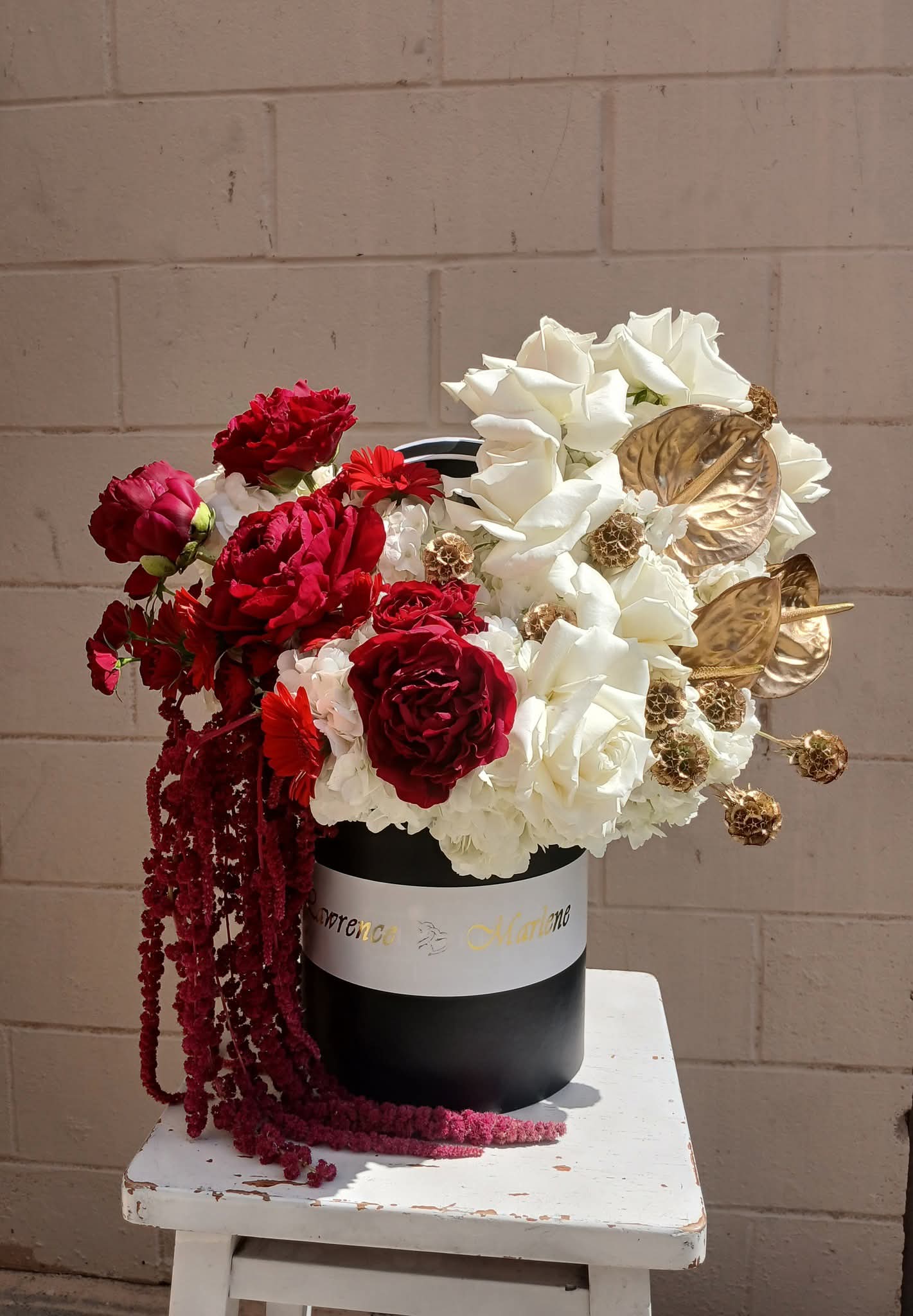 Flower arrangement with red and white flowers in a black and white vase on a white table against a brick wall.